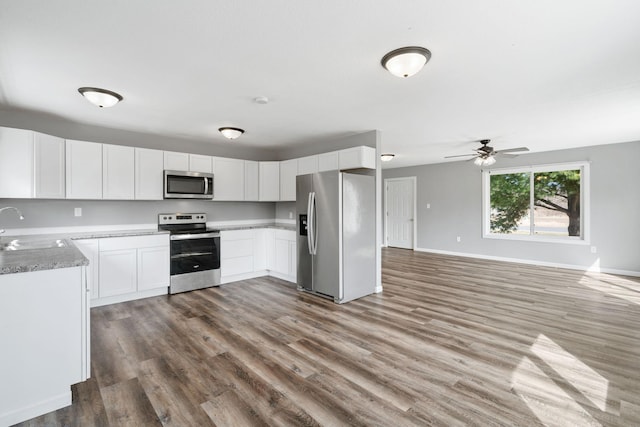 kitchen with a sink, open floor plan, wood finished floors, ceiling fan, and appliances with stainless steel finishes