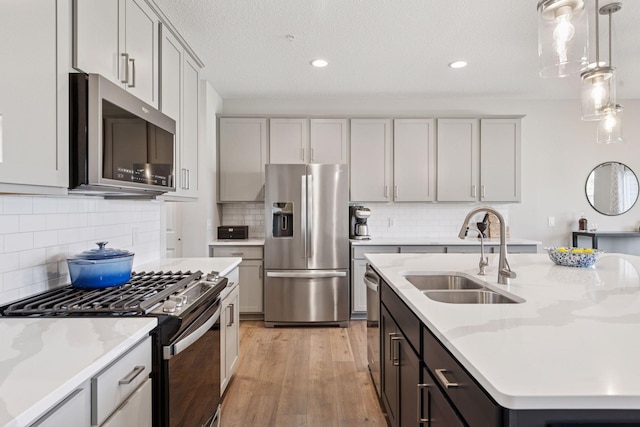 kitchen with a sink, decorative backsplash, an island with sink, stainless steel appliances, and light wood-style flooring