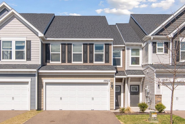 townhome / multi-family property with an attached garage, roof with shingles, and driveway