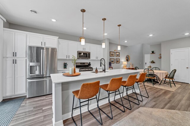 22962 Hazel Ln, Rogers, MN 55374 - kitchen featuring appliances with stainless steel finishes, white cabinets, light wood finished floors, a kitchen breakfast bar, and an island with sink