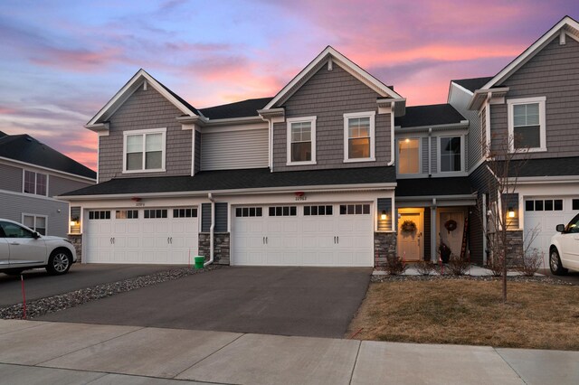 22962 Hazel Ln, Rogers, MN 55374 - townhome / multi-family property with stone siding, a garage, driveway, and a shingled roof