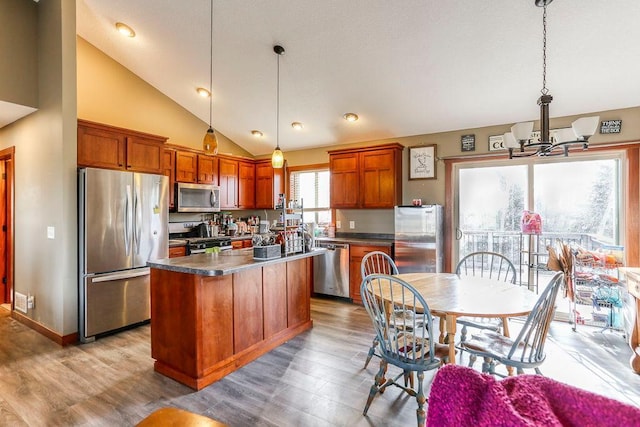 kitchen with stainless steel appliances, a kitchen island, dark countertops, light wood-style floors, and a notable chandelier
