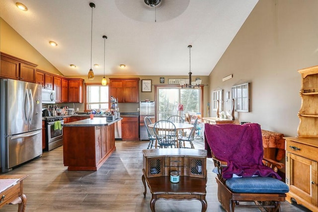 kitchen featuring dark wood-style flooring, stainless steel appliances, dark countertops, pendant lighting, and a center island