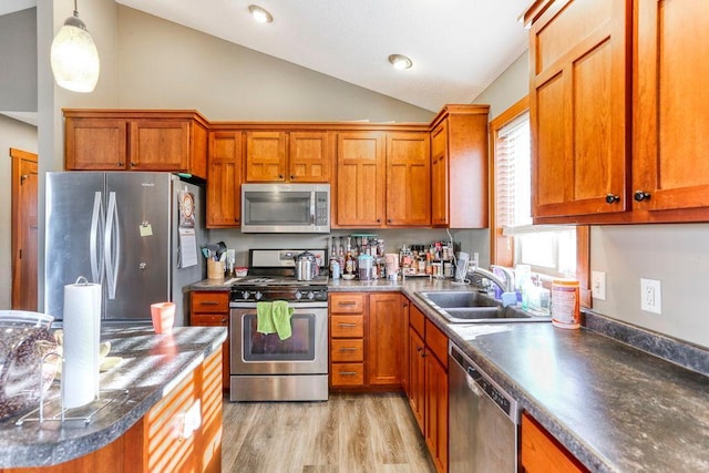 kitchen with vaulted ceiling, a sink, light wood finished floors, appliances with stainless steel finishes, and brown cabinetry