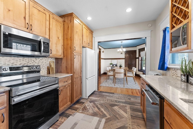 kitchen featuring light stone counters, decorative backsplash, stainless steel appliances, a notable chandelier, and recessed lighting