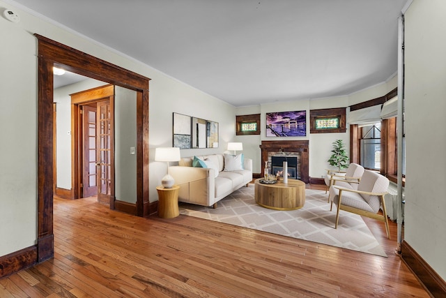living room with hardwood / wood-style floors, a stone fireplace, a healthy amount of sunlight, ornamental molding, and baseboards