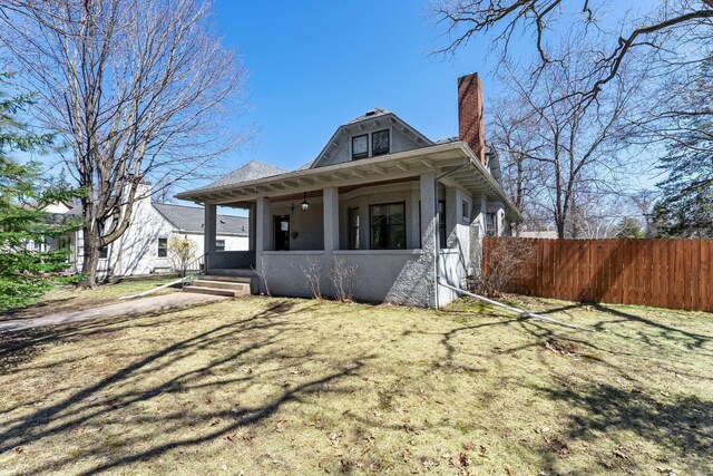 view of front facade with stucco siding, a porch, a chimney, and fence