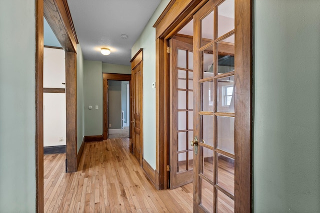 hallway with light wood-type flooring, french doors, and baseboards