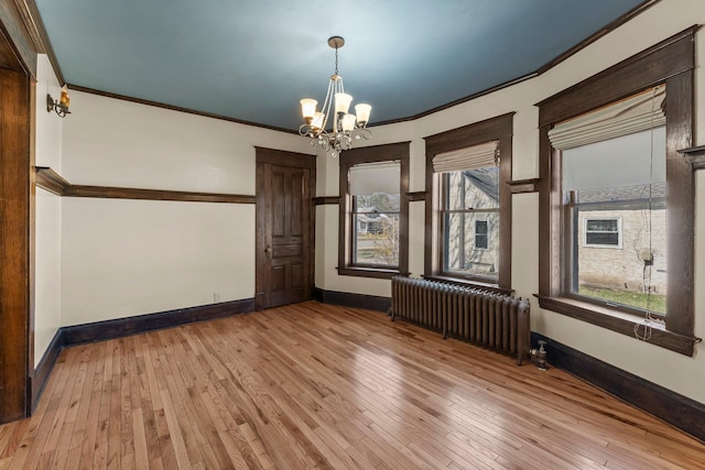 empty room with radiator, light wood-type flooring, baseboards, an inviting chandelier, and ornamental molding