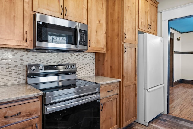 kitchen with light stone countertops, stainless steel appliances, dark wood-type flooring, and tasteful backsplash