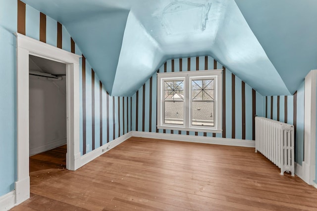 bonus room featuring wallpapered walls, radiator heating unit, lofted ceiling, baseboards, and hardwood / wood-style flooring