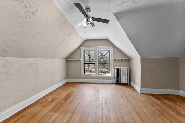 bonus room featuring lofted ceiling, hardwood / wood-style flooring, baseboards, and radiator