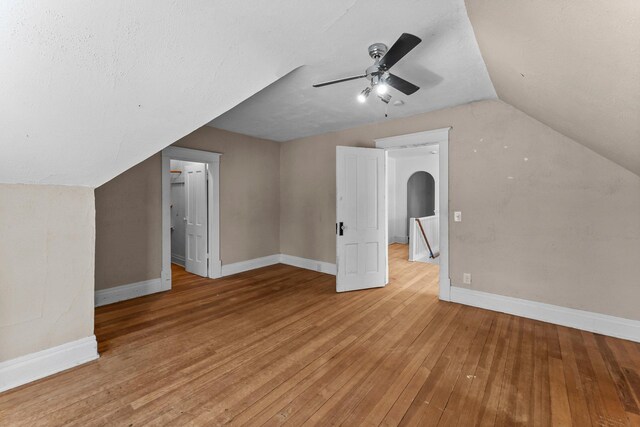 bonus room featuring vaulted ceiling, ceiling fan, arched walkways, light wood-style flooring, and baseboards