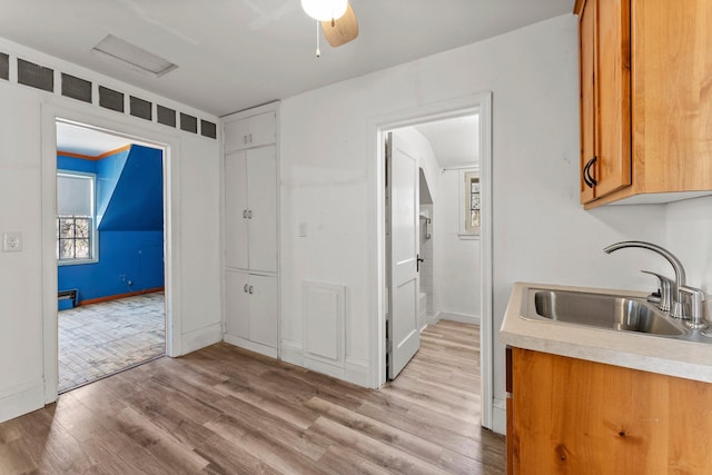 kitchen featuring light countertops, a sink, light wood-type flooring, baseboards, and brown cabinetry