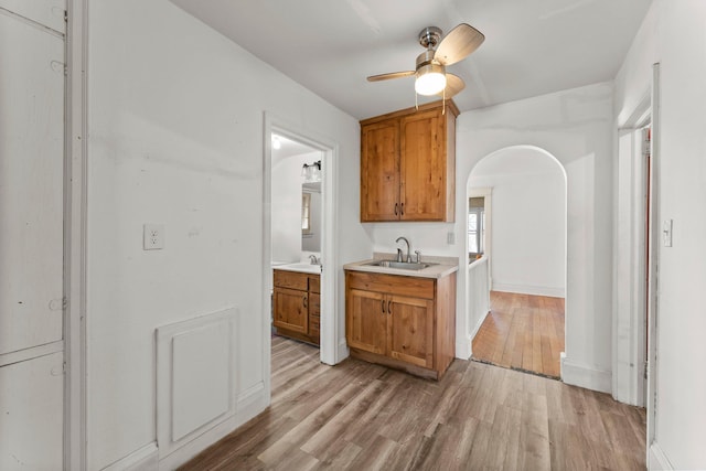 kitchen with brown cabinetry, light wood-type flooring, ceiling fan, and a sink