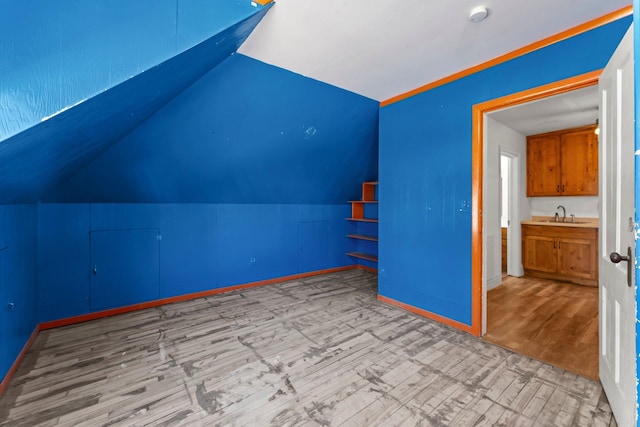 additional living space with lofted ceiling, wood finished floors, baseboards, and a sink