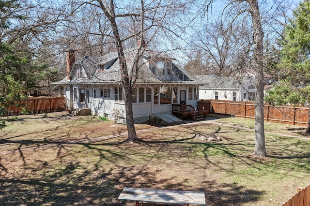 rear view of property featuring a chimney, a fenced backyard, a wooden deck, a lawn, and a sunroom