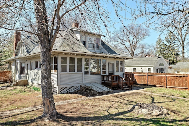 back of property featuring a chimney, a deck, fence, roof with shingles, and a sunroom