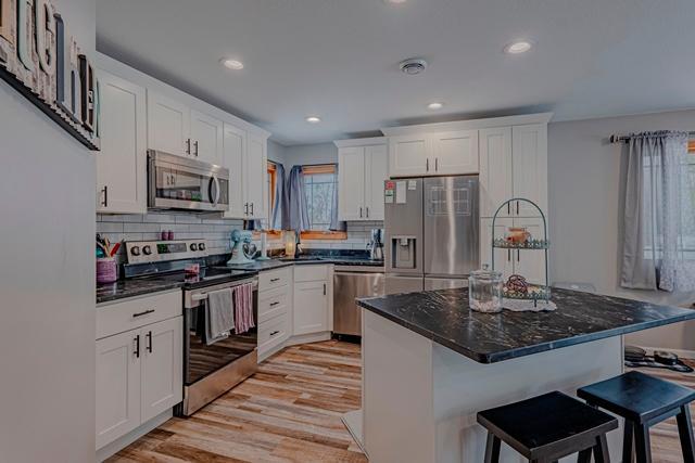 20371 Golf Crest Dr, Grand Rapids, MN 55744 - kitchen with stainless steel appliances, a kitchen breakfast bar, white cabinets, light wood-style flooring, and decorative backsplash
