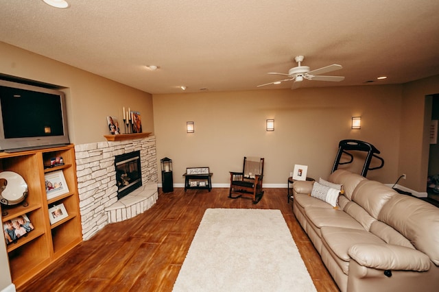 241 Cottonwood Cv, Lynd, MN 56157 - living room featuring dark wood-type flooring, baseboards, a textured ceiling, ceiling fan, and a stone fireplace