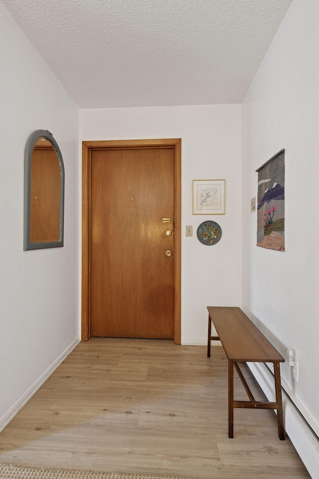hallway featuring baseboards, a textured ceiling, and light wood finished floors