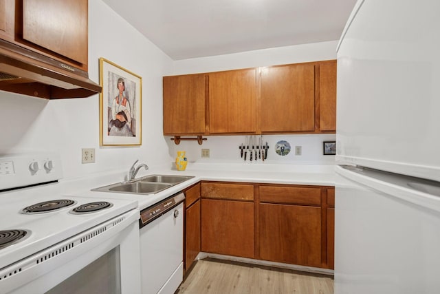 kitchen featuring brown cabinets, a sink, light countertops, under cabinet range hood, and white appliances