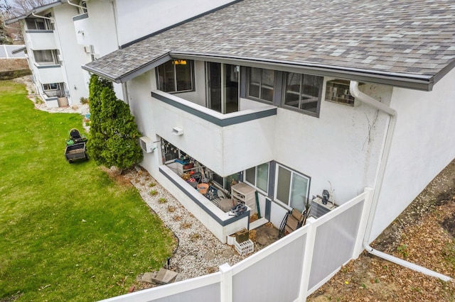 back of property with a lawn, roof with shingles, stucco siding, and fence