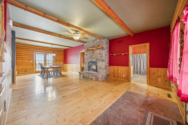 unfurnished living room with beamed ceiling, visible vents, a stone fireplace, wainscoting, and hardwood / wood-style flooring