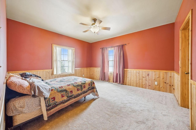 bedroom featuring wood walls, carpet flooring, ceiling fan, and a wainscoted wall