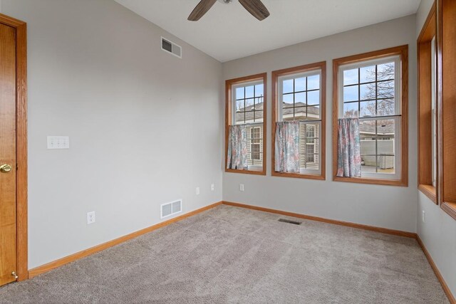 spare room featuring healthy amount of natural light, light colored carpet, and a ceiling fan