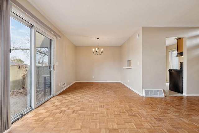 unfurnished room with visible vents, baseboards, and a chandelier
