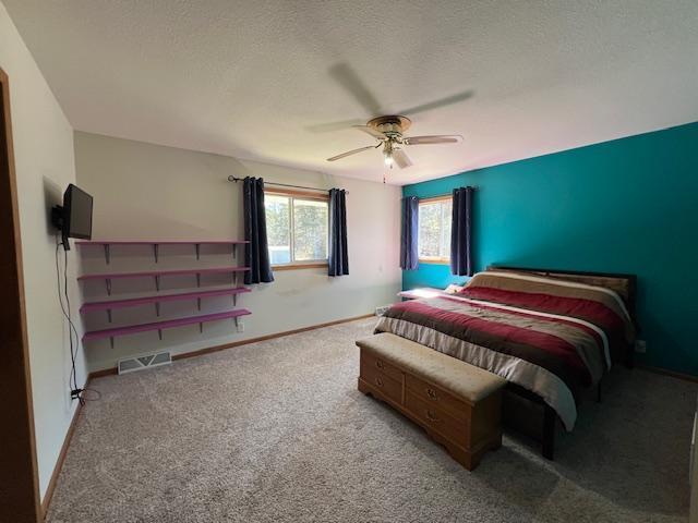 carpeted bedroom with a textured ceiling, visible vents, ceiling fan, and baseboards
