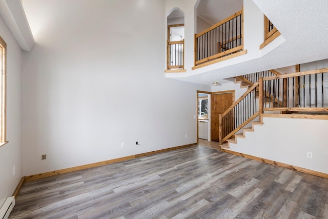 1607 7th Ave, Grand Rapids, MN 55744 - unfurnished living room featuring stairs, wood finished floors, baseboards, a high ceiling, and a baseboard heating unit