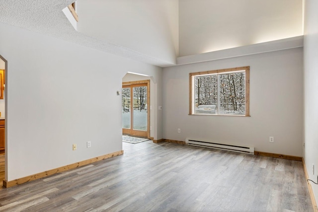 1607 7th Ave, Grand Rapids, MN 55744 - unfurnished room with a baseboard radiator, arched walkways, wood finished floors, baseboards, and lofted ceiling