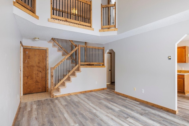 1607 7th Ave, Grand Rapids, MN 55744 - unfurnished living room featuring a towering ceiling, wood finished floors, arched walkways, baseboards, and stairs