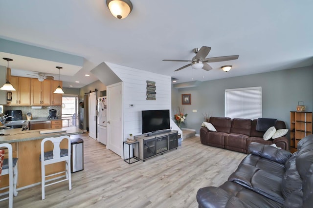 living area featuring a barn door, baseboards, a ceiling fan, and light wood-style flooring