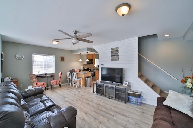 living area featuring baseboards, a ceiling fan, wood finished floors, and stairs