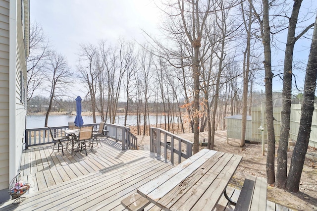 deck with outdoor dining area, an outdoor structure, a water view, and a storage unit