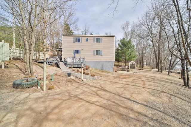 rear view of property with fence, a storage unit, an outbuilding, and a deck