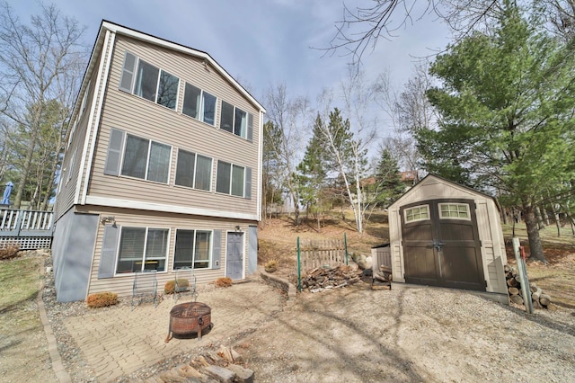 back of house with a deck, a fire pit, an outbuilding, and a shed