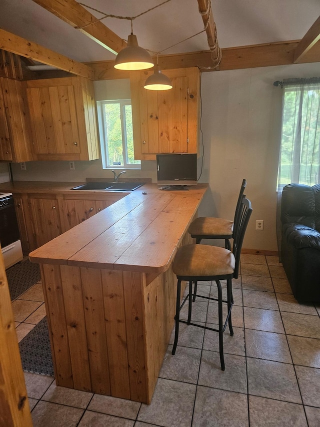 kitchen with a peninsula, light brown cabinetry, a sink, and stove