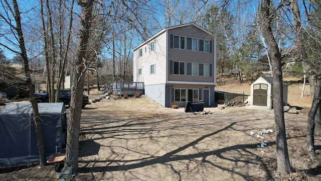 back of property featuring a storage shed, an outbuilding, a wooden deck, and driveway
