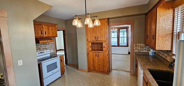 502 Park St S, Fairfax, MN 55332 - kitchen with white electric range oven, brown cabinetry, backsplash, under cabinet range hood, and a chandelier