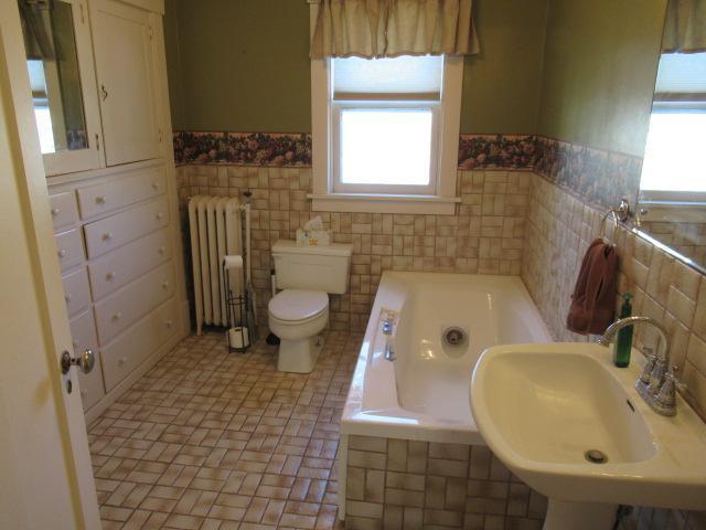502 Park St S, Fairfax, MN 55332 - bathroom featuring radiator, a sink, tile walls, a wainscoted wall, and a garden tub