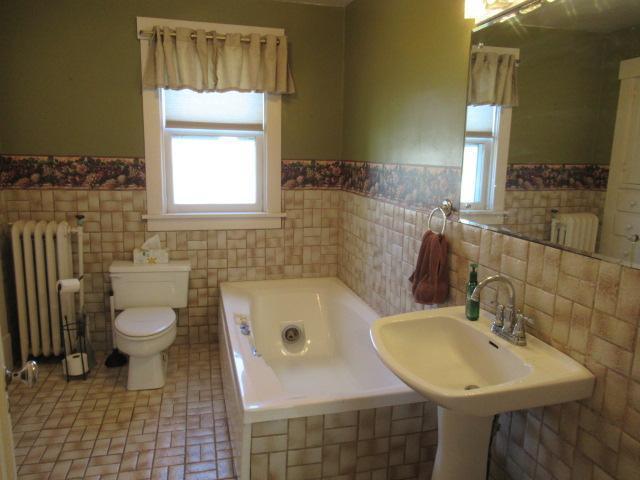 502 Park St S, Fairfax, MN 55332 - bathroom with radiator, a garden tub, toilet, wainscoting, and tile walls