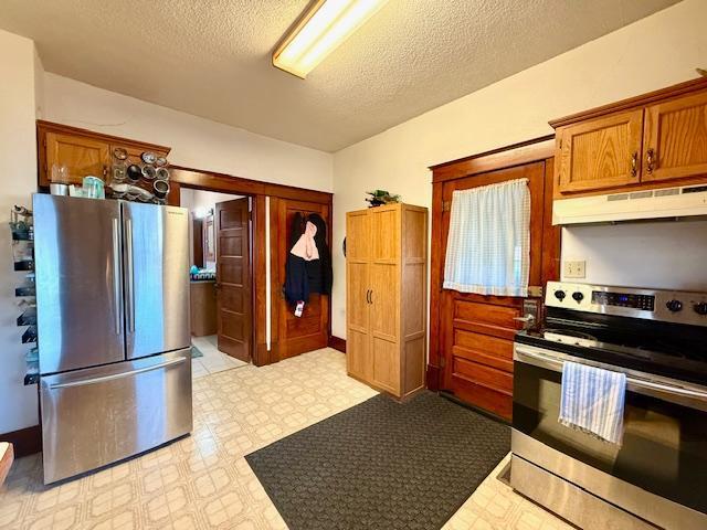kitchen featuring stainless steel appliances, under cabinet range hood, a textured ceiling, brown cabinetry, and light floors
