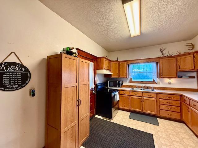 kitchen featuring stainless steel microwave, light floors, a sink, range with electric stovetop, and brown cabinetry