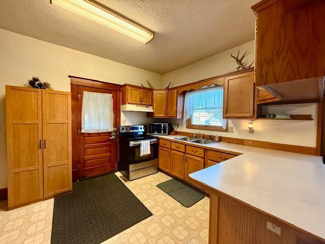 kitchen featuring under cabinet range hood, a sink, appliances with stainless steel finishes, brown cabinetry, and light floors