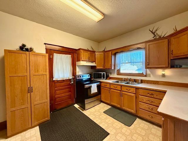 kitchen with brown cabinets, light floors, appliances with stainless steel finishes, under cabinet range hood, and a sink