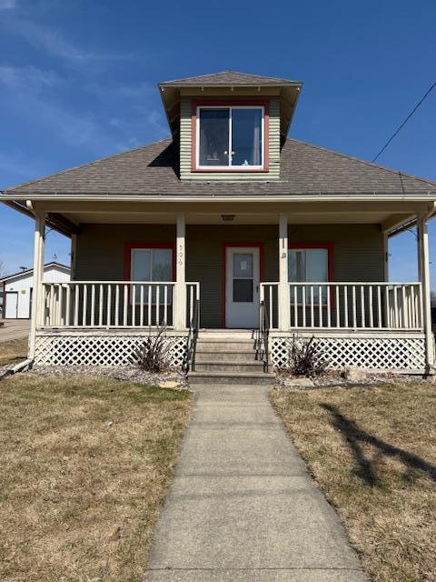 view of front facade featuring a shingled roof, a front lawn, and a porch